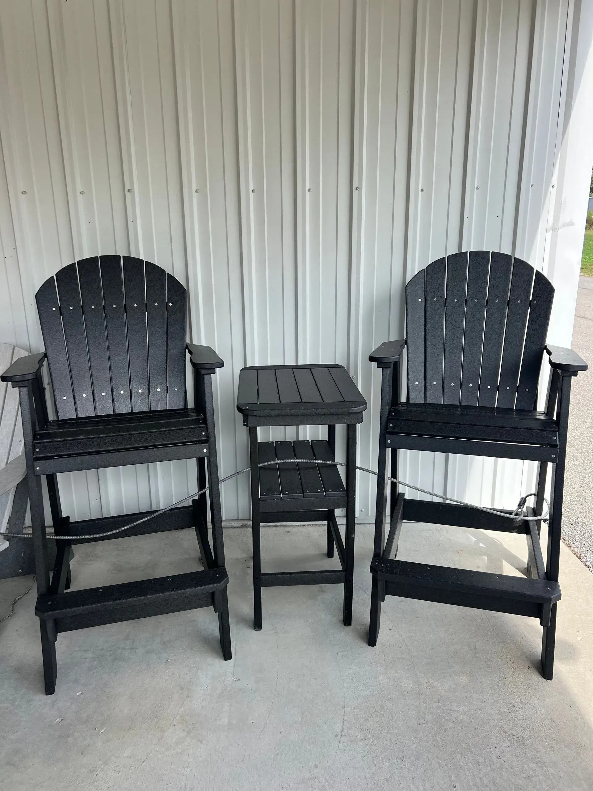 Two black Adirondack-style bar chairs and a small table on a porch.