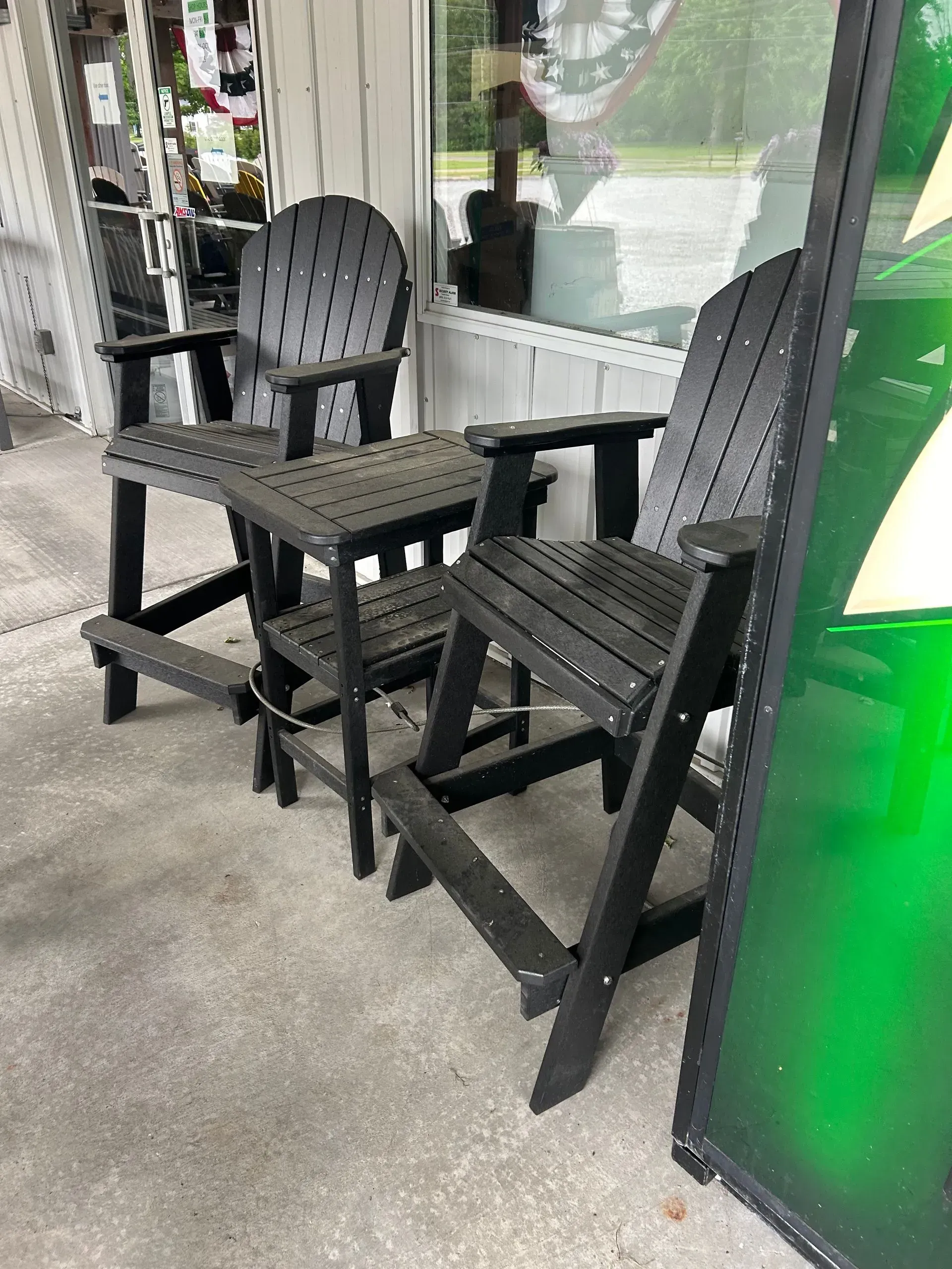Black outdoor Adirondack chairs and a small table on a concrete patio.
