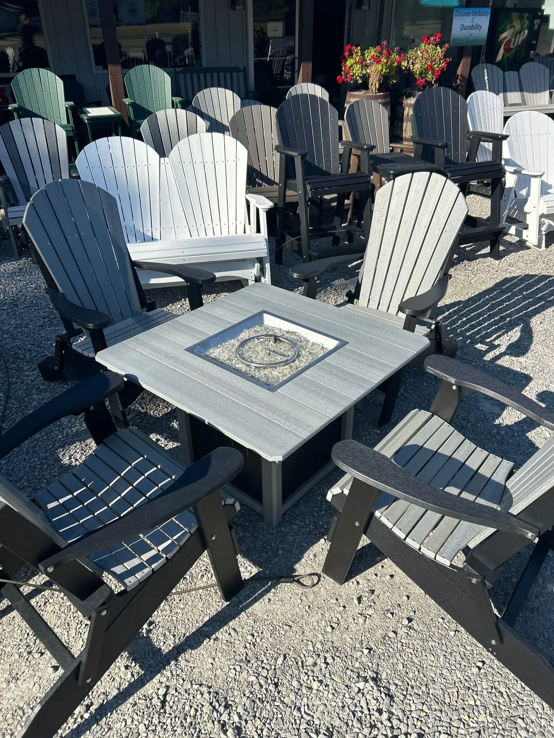Outdoor patio set with fire pit, four Adirondack chairs, gray and black, gravel ground.
