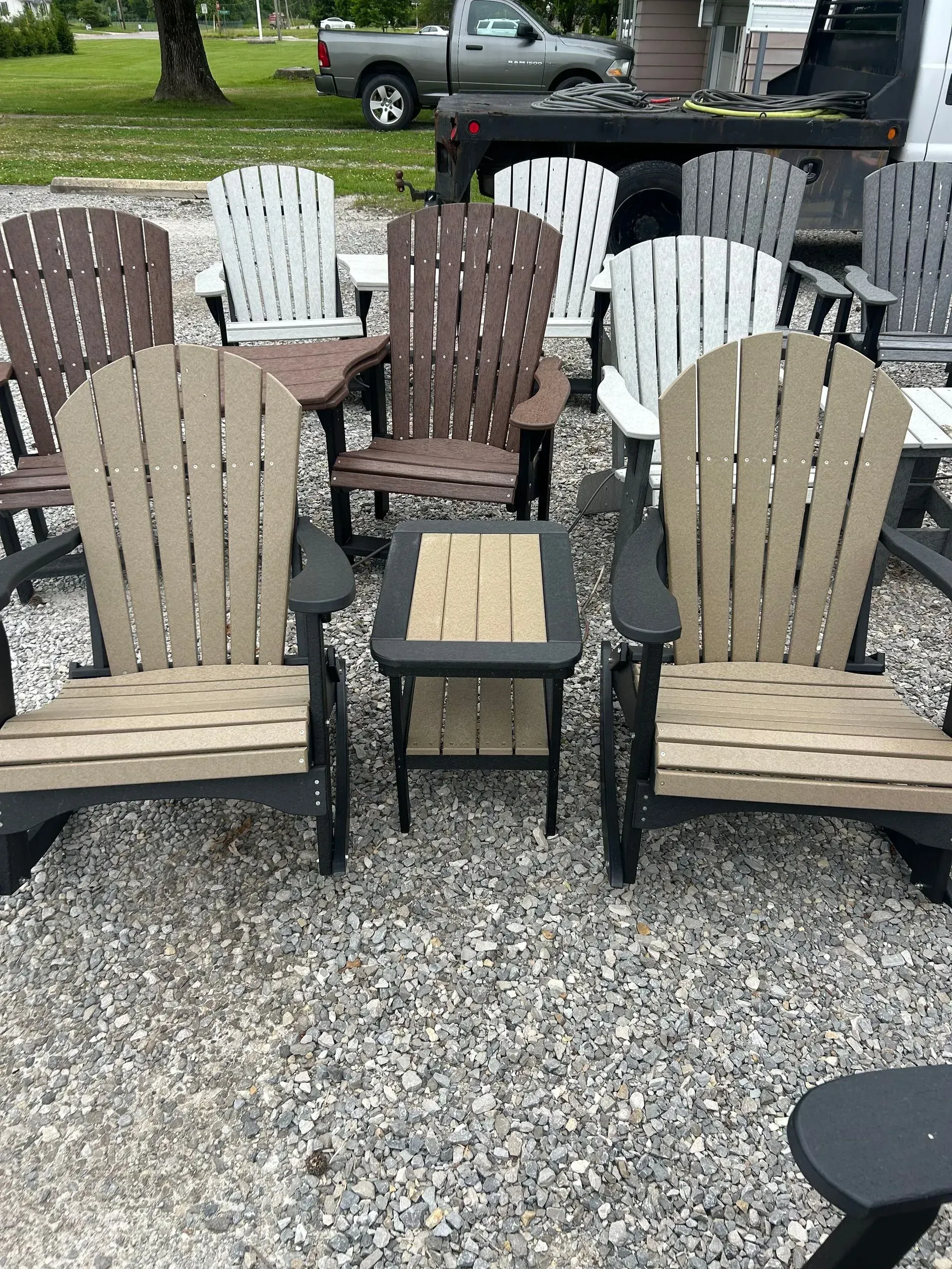 Adirondack chairs in various colors around a small table, displayed outside on gravel.