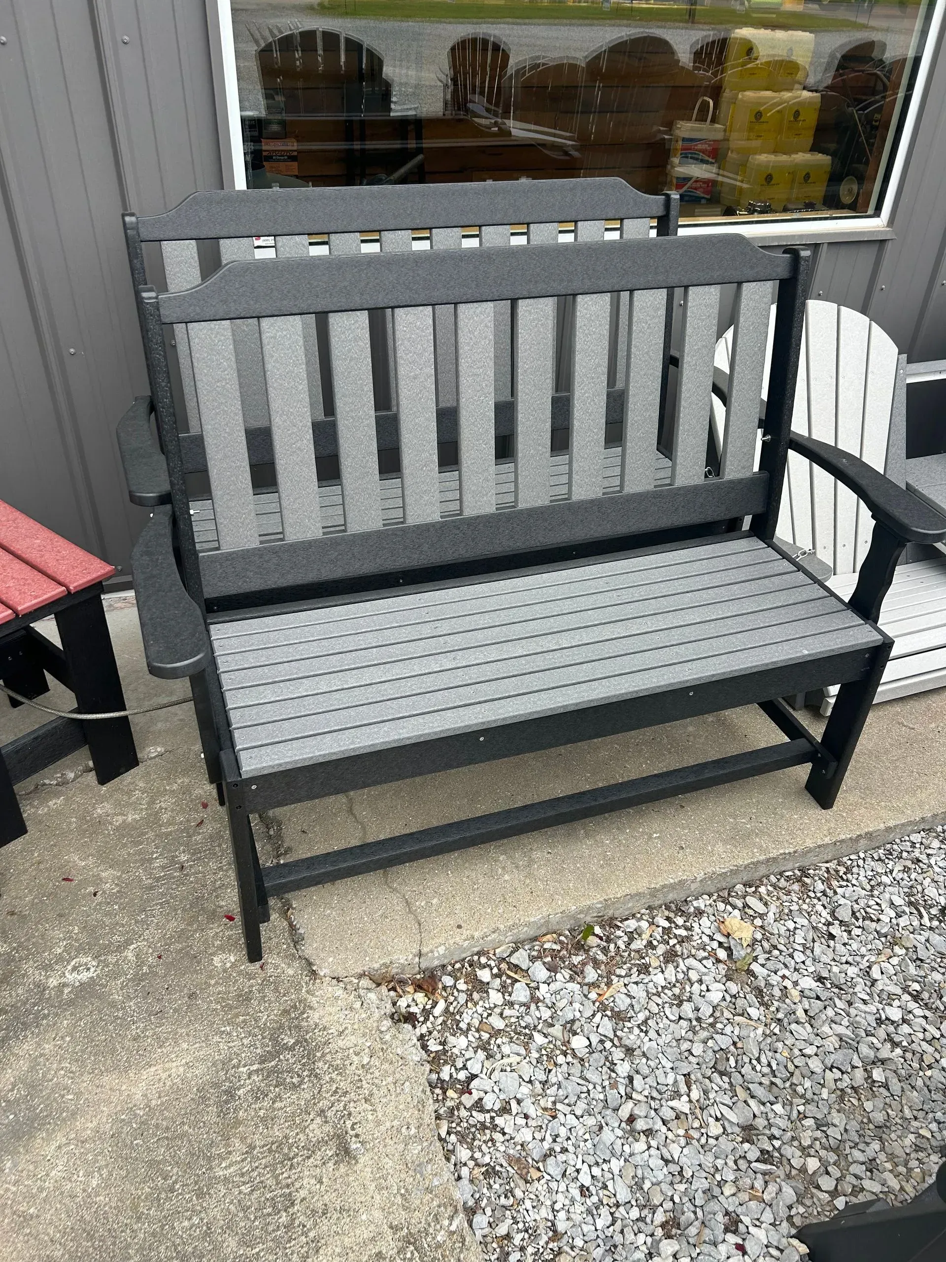 Black and gray outdoor bench with vertical back slats and a textured seat, on a concrete surface.