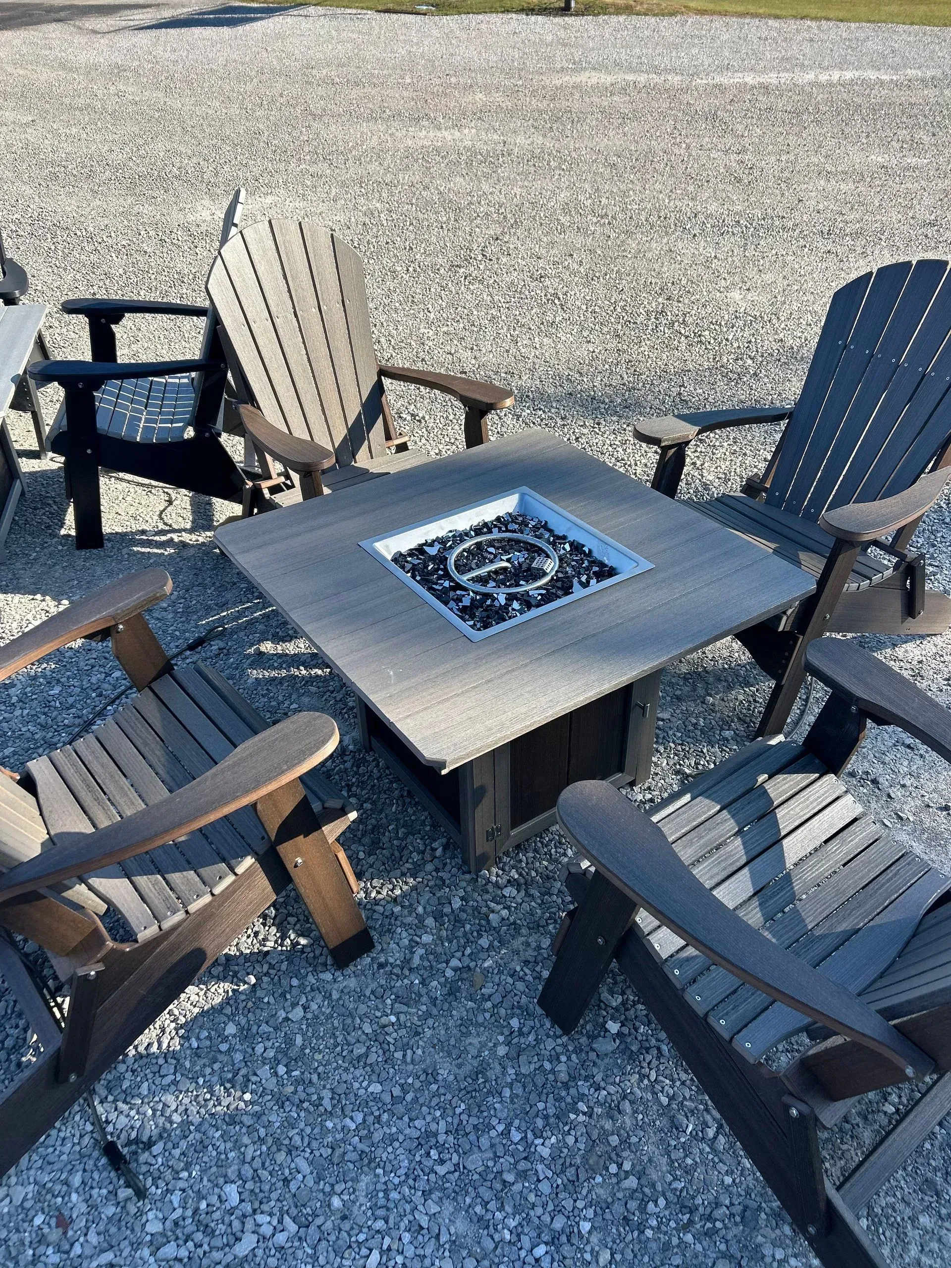 Outdoor seating arrangement with a fire pit table and four Adirondack chairs.