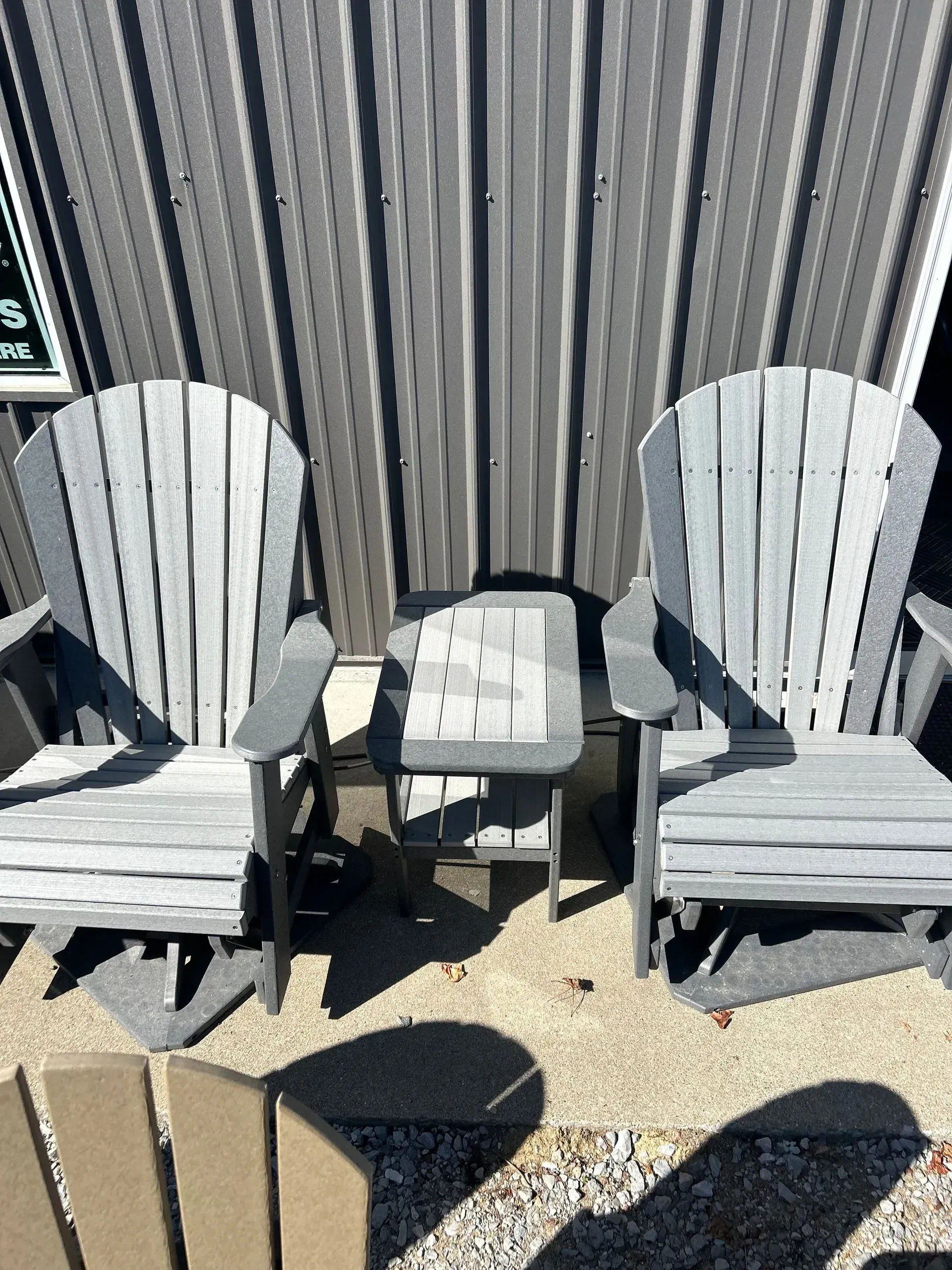 Two gray Adirondack chairs and a small table sit in front of a corrugated wall.