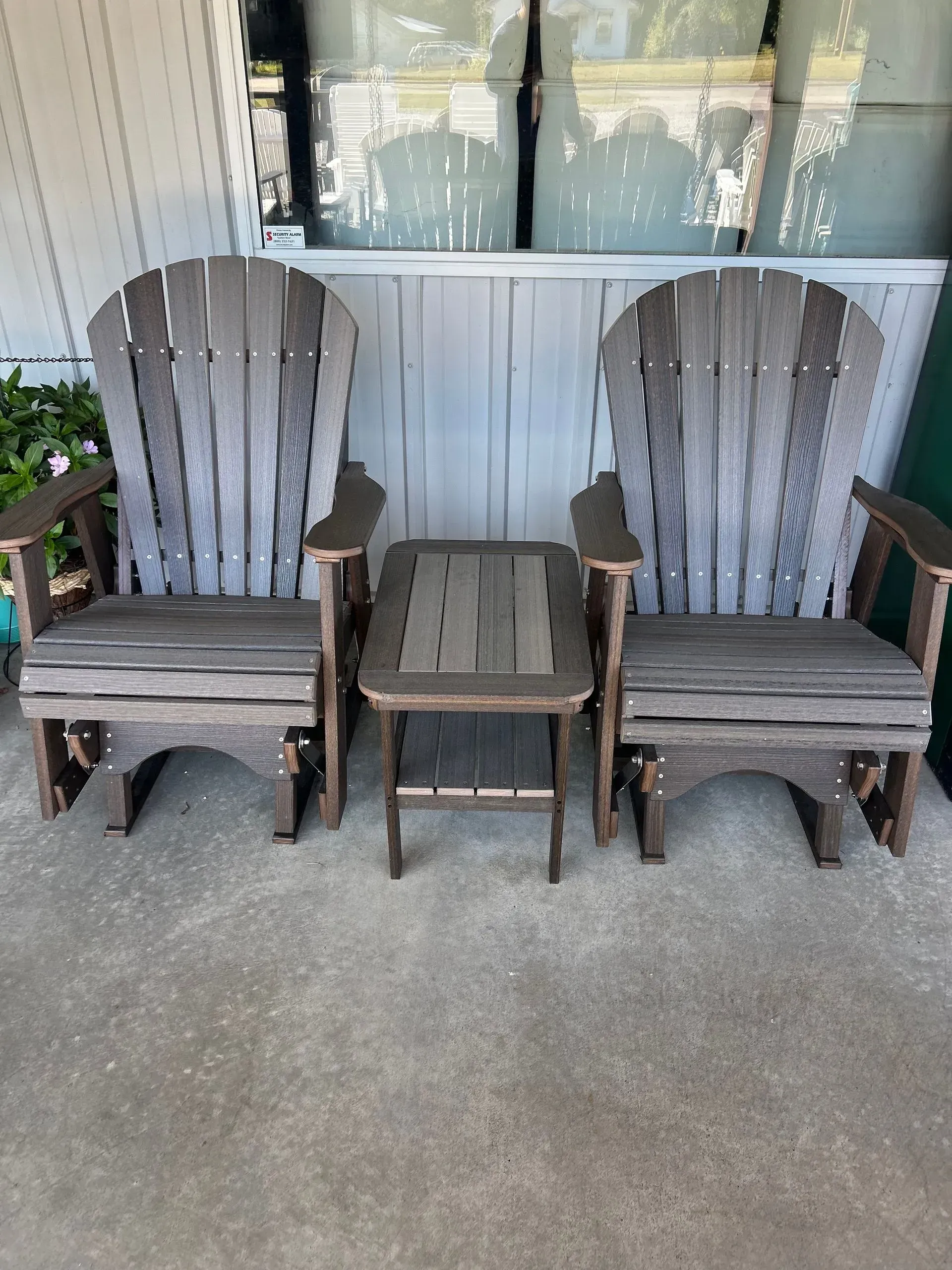 Two Adirondack-style gray glider chairs with a matching side table, set on a patio.