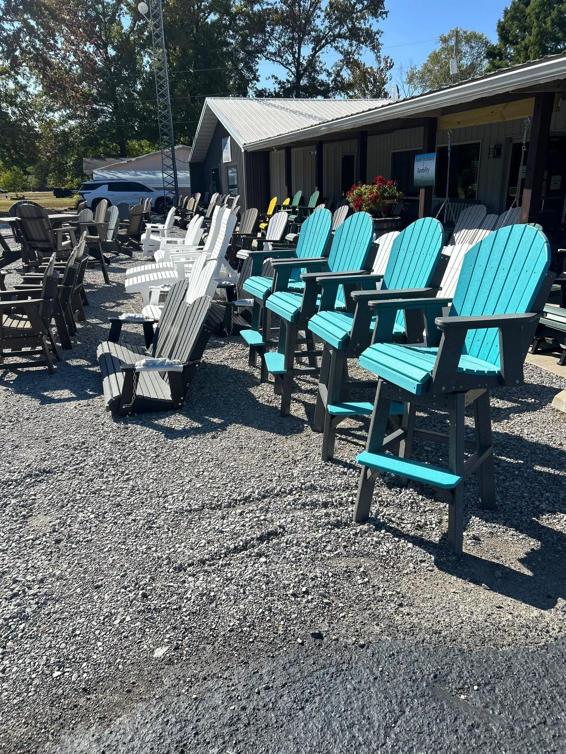 Outdoor chairs displayed outside a store, various colors including teal and white. Gravel ground.