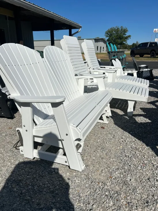 White outdoor glider chairs in a gravel lot, under a sunny sky.