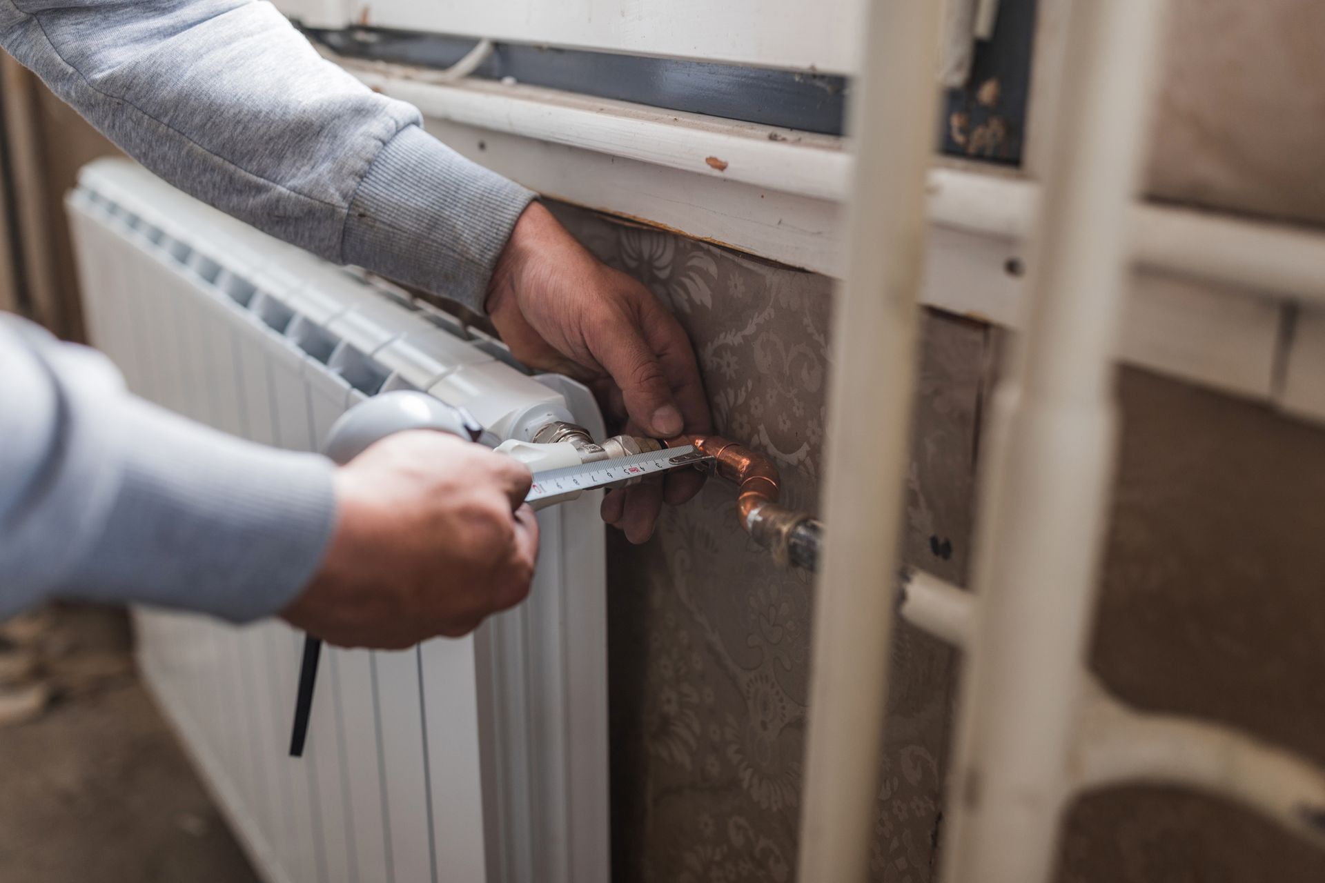 A man is measuring a radiator with a tape measure.
