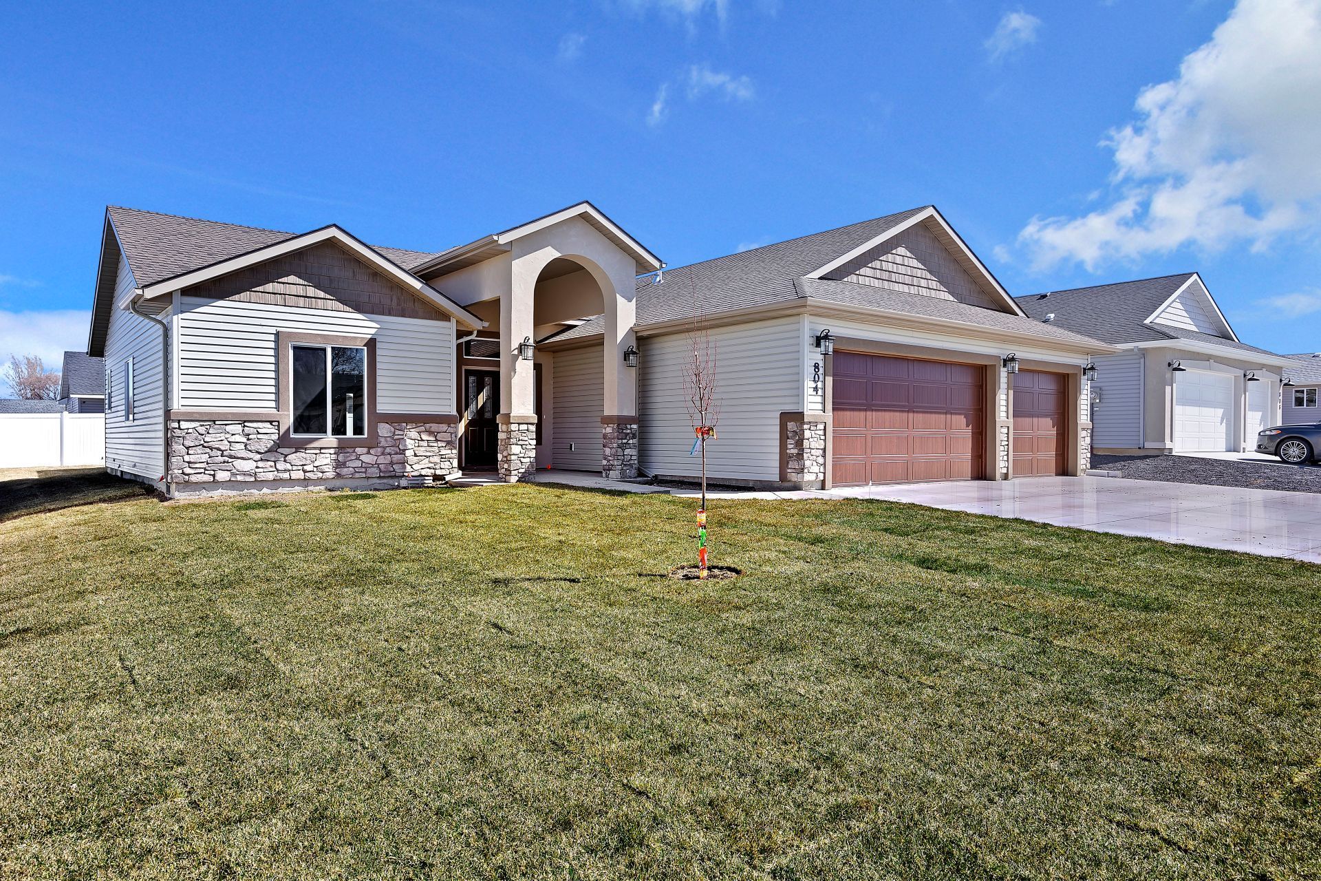 Ranch-style house with three-car garage, brown garage doors, and stone accents under a blue sky.
