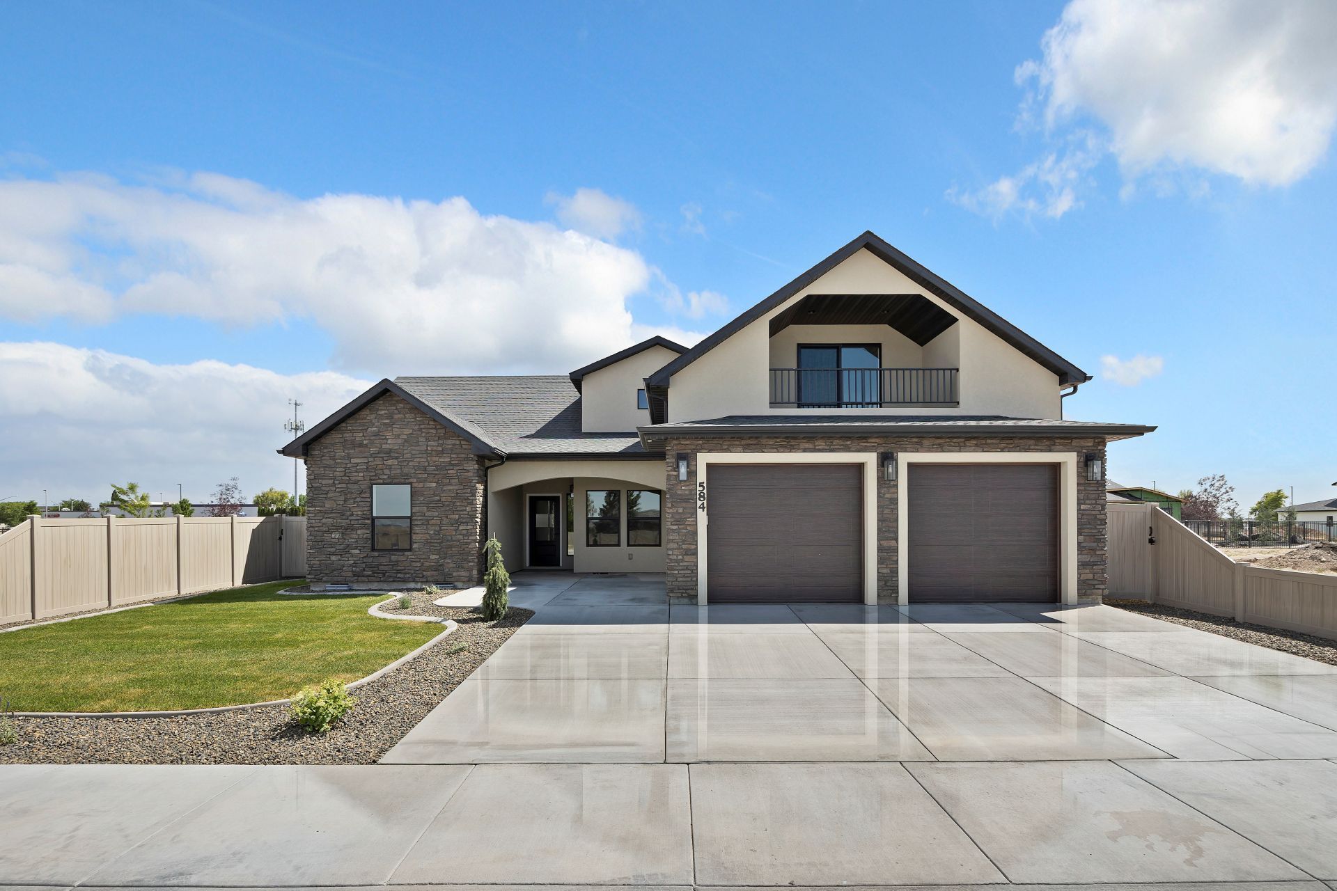 Two-story house with a brick and stucco facade, two-car garage, and a balcony, under a blue sky.