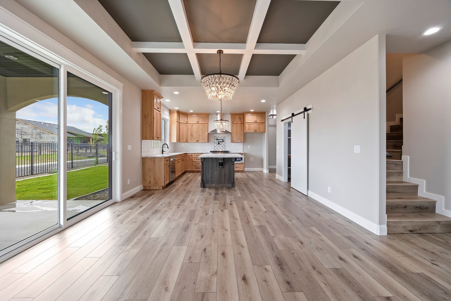Spacious, modern kitchen and living area with hardwood floors, a sliding glass door, and a chandelier.