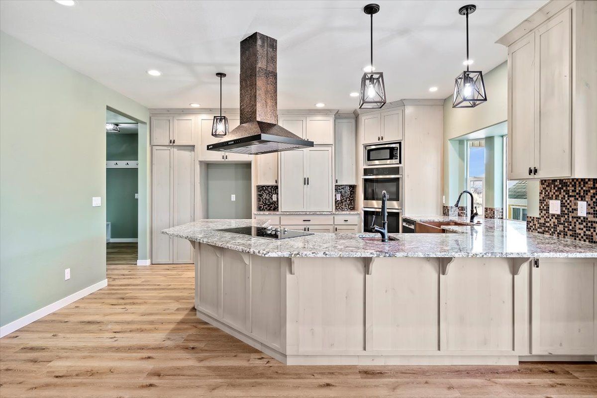 Spacious modern kitchen with light wood floors, white cabinets, granite island, and stainless steel appliances.