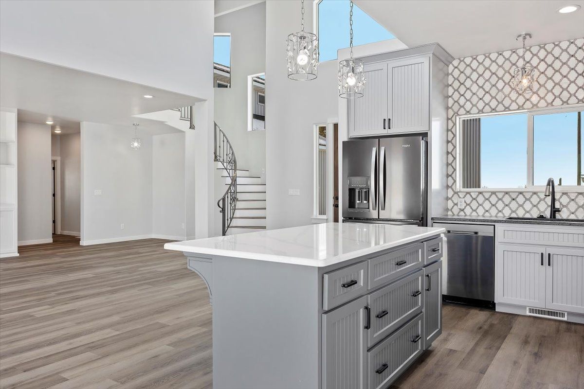 Modern kitchen with island, stainless steel appliances, and white cabinets. Light gray walls, wood floors.