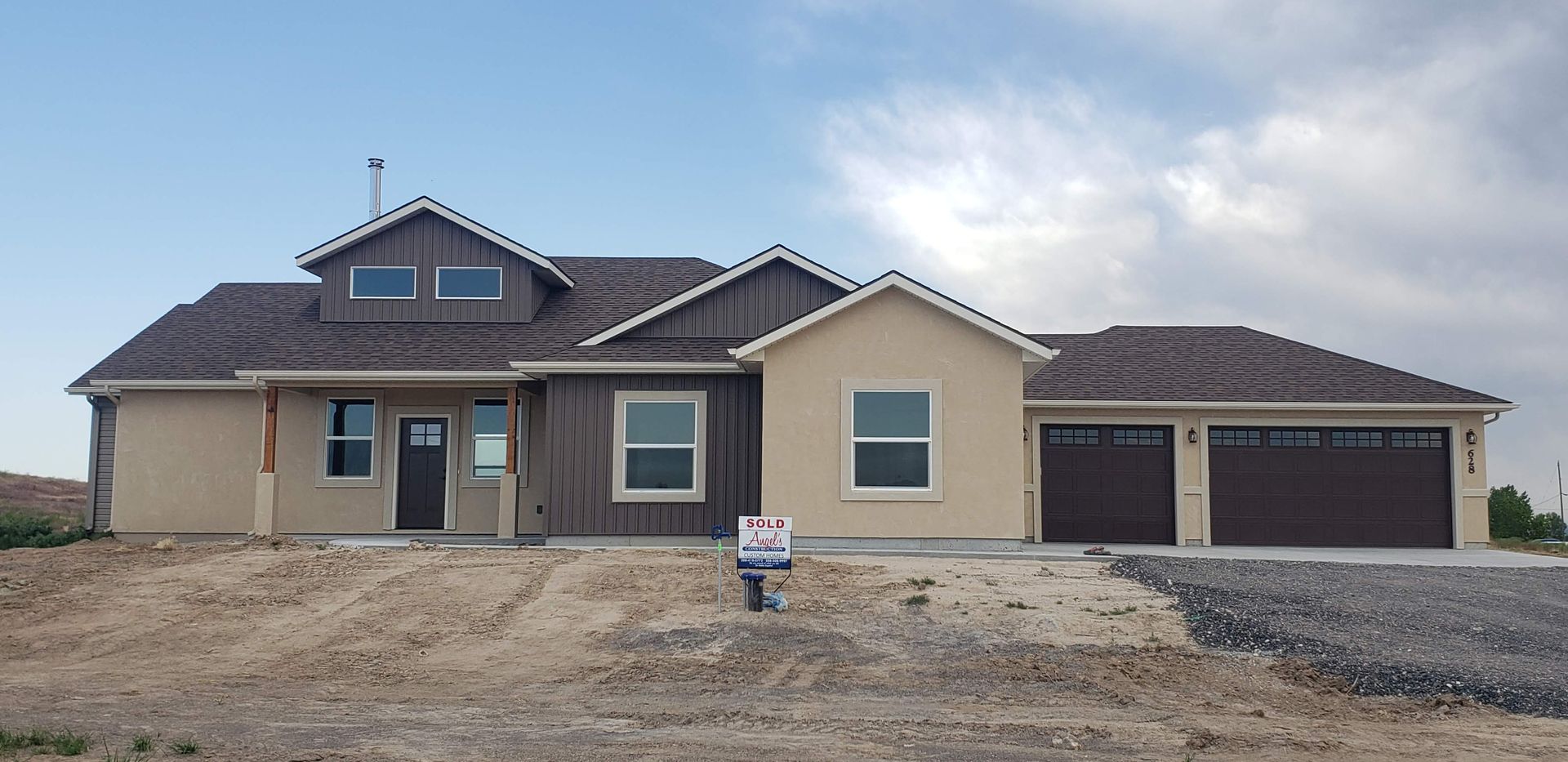 New home construction. Tan stucco and brown siding. Brown roof and garage doors. Cloudy sky.