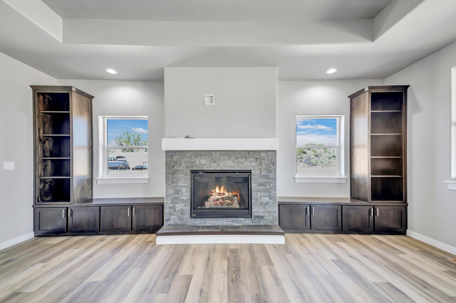 Living room with fireplace, built-in shelves, and windows. Gray walls, wooden floors, and dark cabinetry.