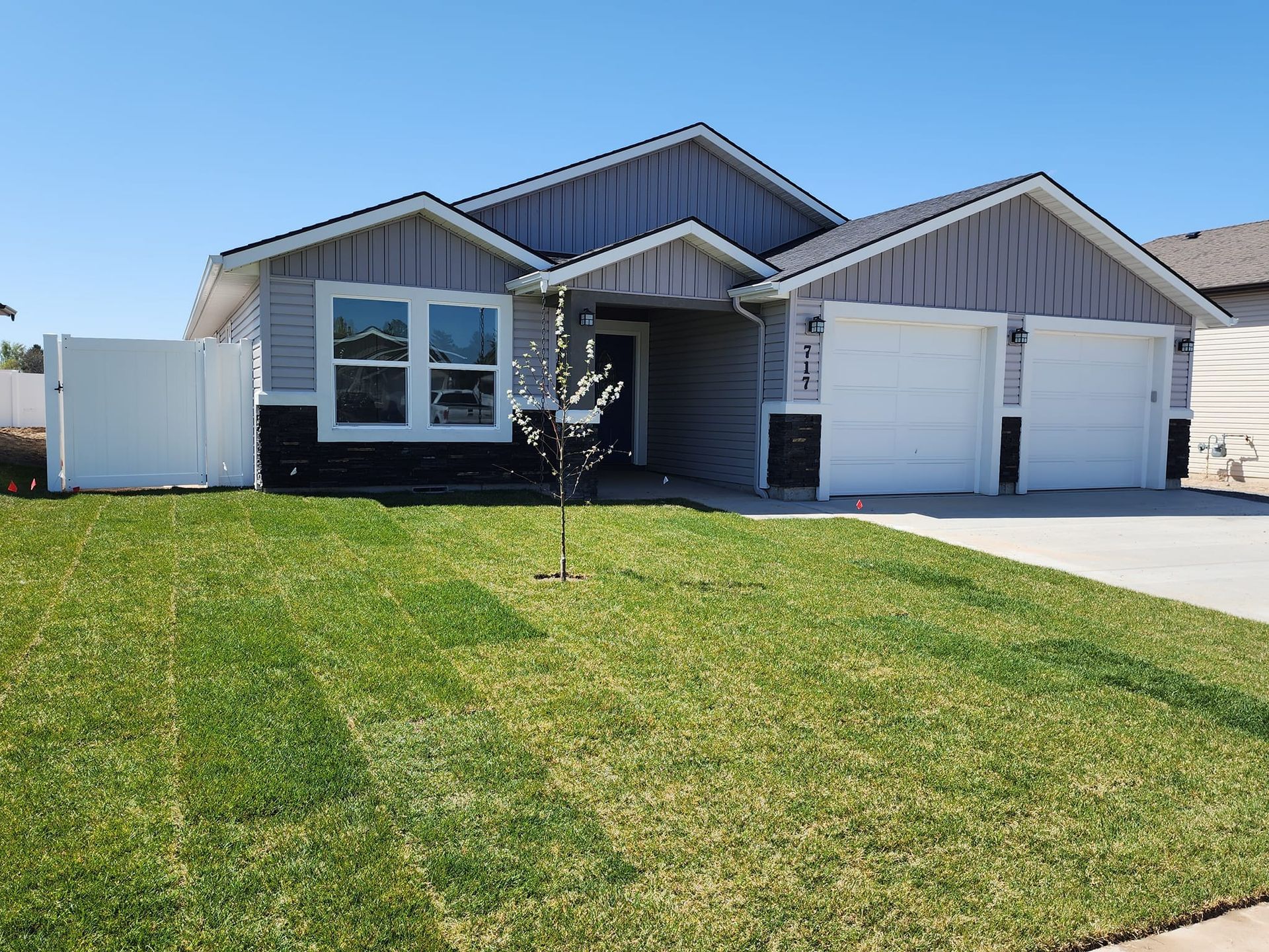 A single-story house with gray siding, a two-car garage, and a green lawn under a blue sky.