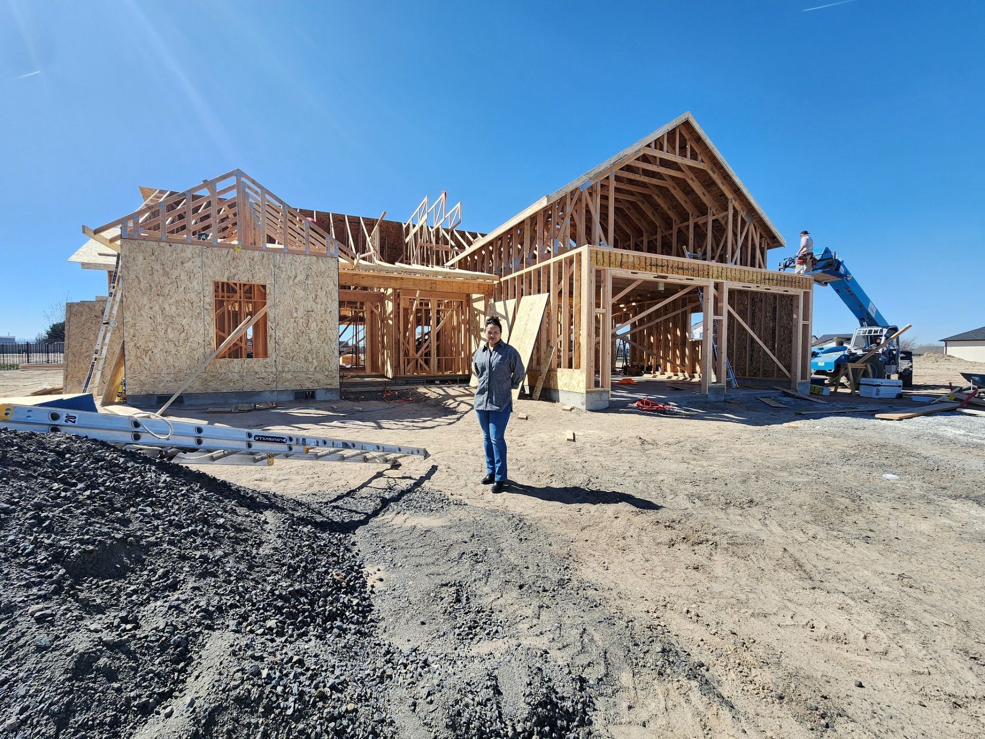 Construction of a wooden house frame, man standing in front on a sunny day.
