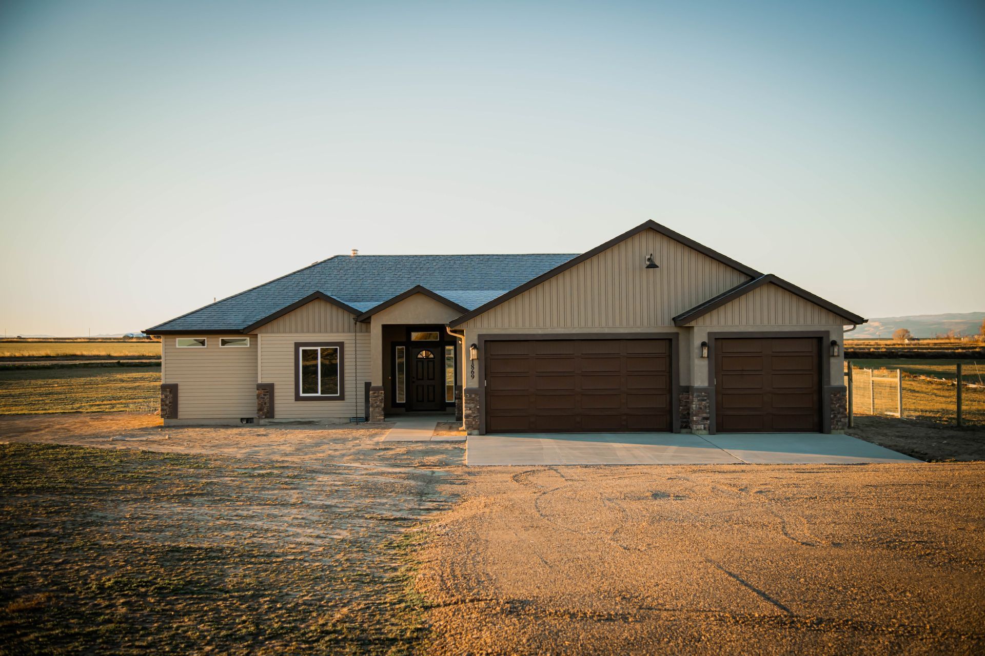 Ranch-style house with two garage doors and a wooden facade. Located on a dirt lot.