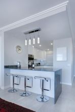 A Clean kitchen with a bar and stools and a clock on the wall.