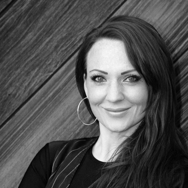 A woman wearing hoop earrings is smiling in a black and white photo. Dana Miller