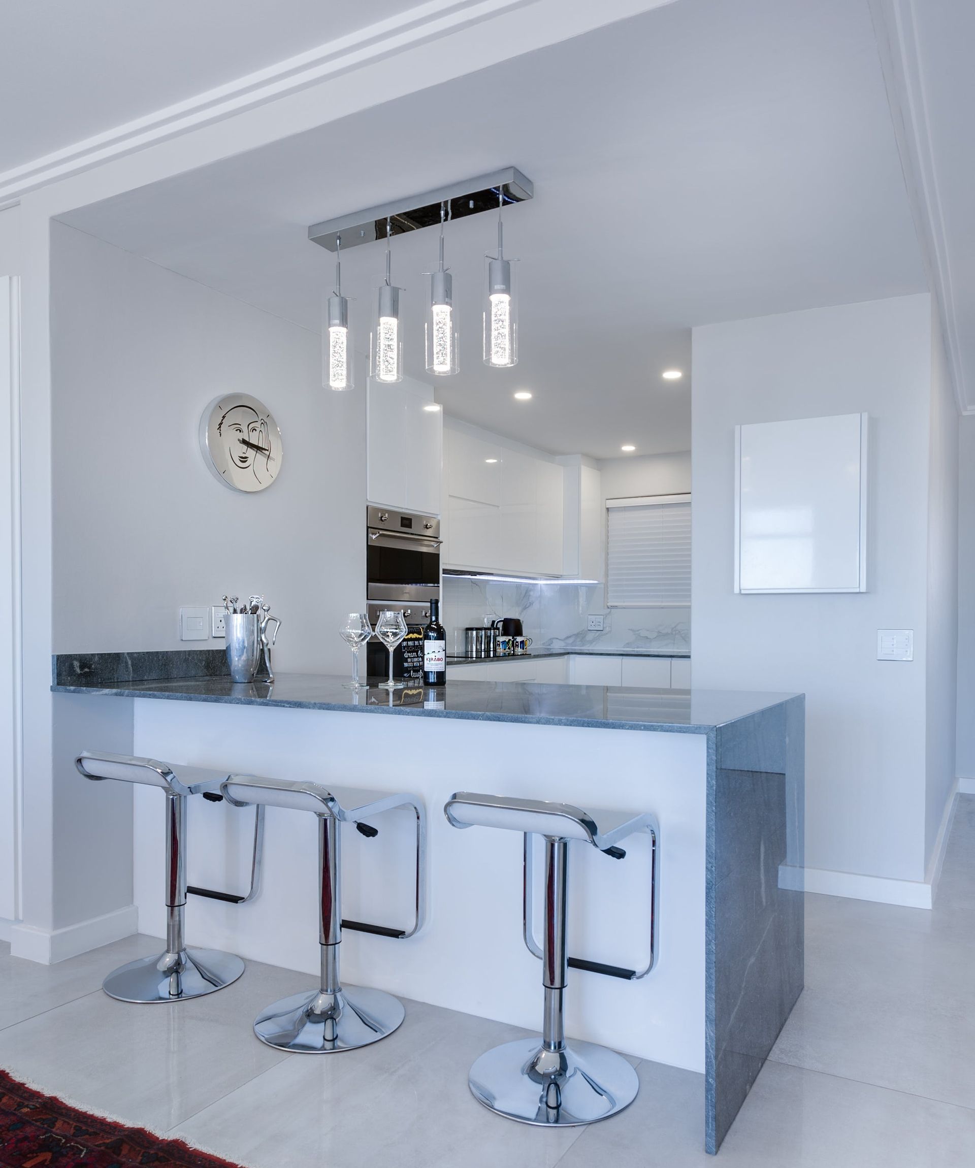 A kitchen with a bar and stools and a clock on the wall