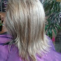 Blonde hair, slightly layered, with a purple shirt, near a green plant.