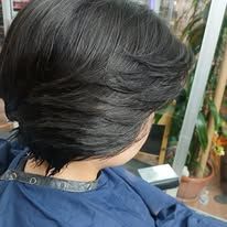 Close-up of a person's dark layered hairstyle, mostly focused on the back of their head, in a blue shirt.