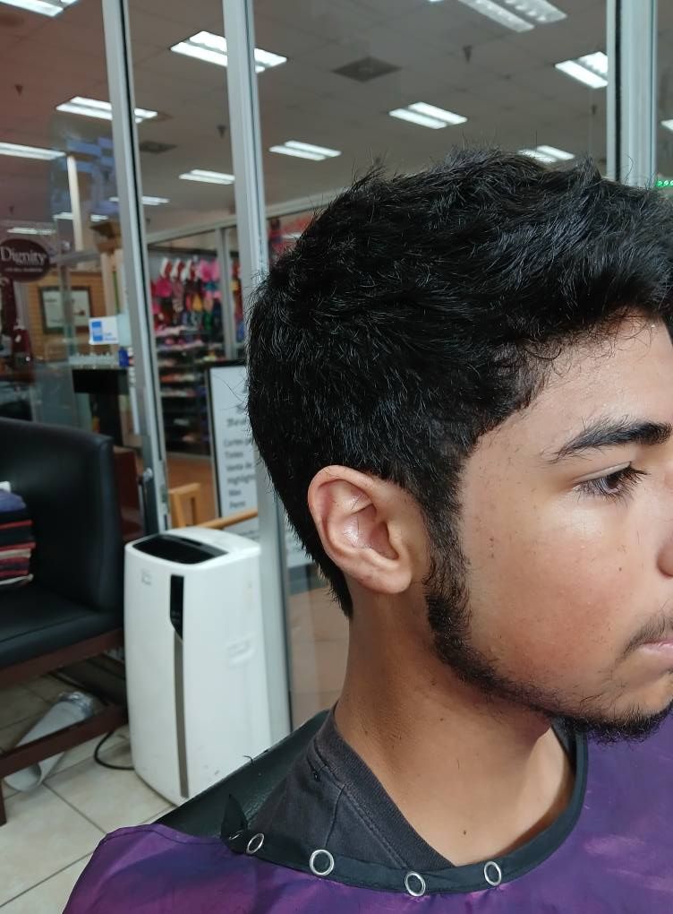 Man with a textured haircut and trimmed beard, seated in a salon, wearing a purple cape.