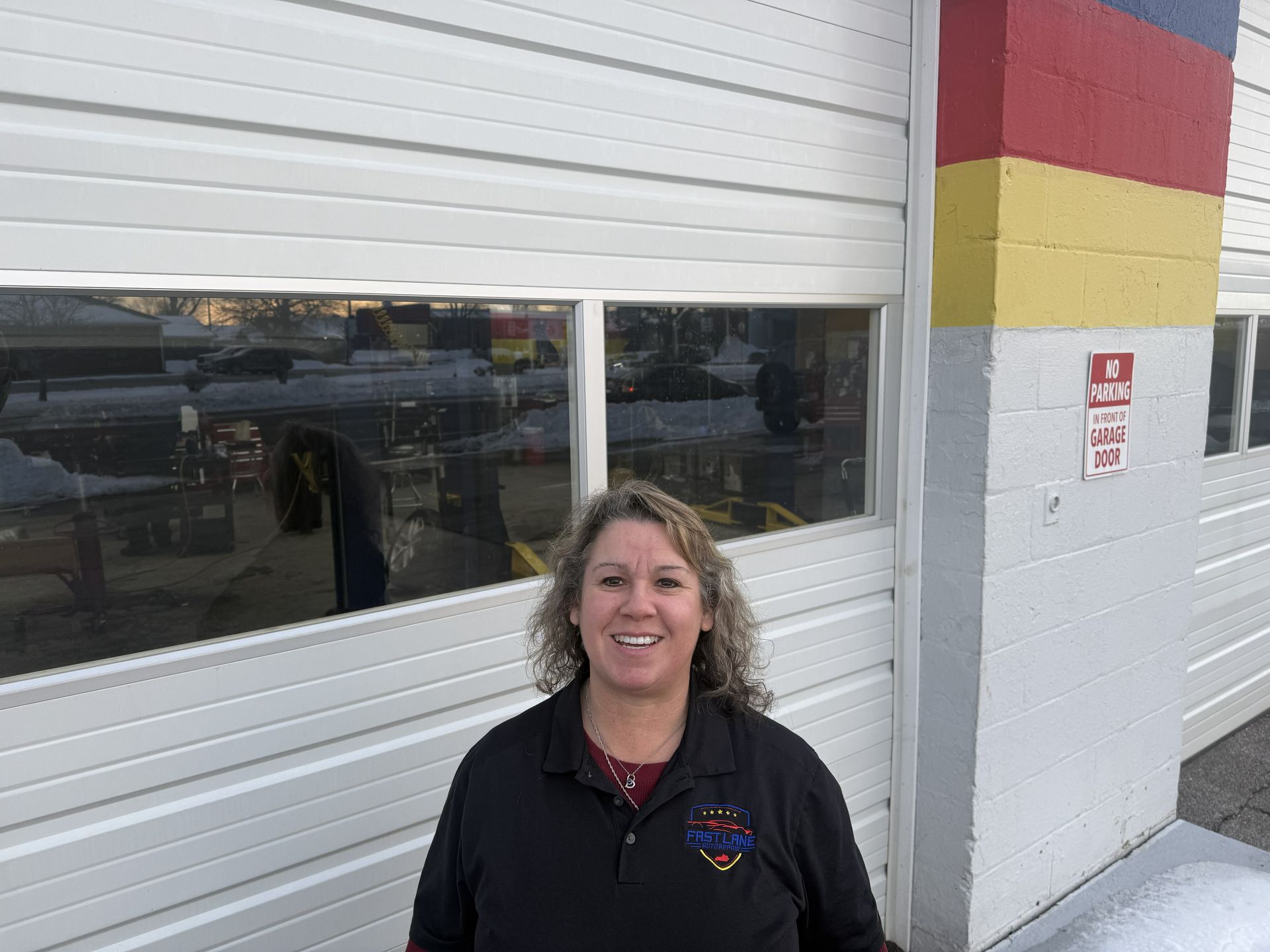 Woman in black jacket smiles in front of a white garage door, next to a red, yellow, and blue painted wall.