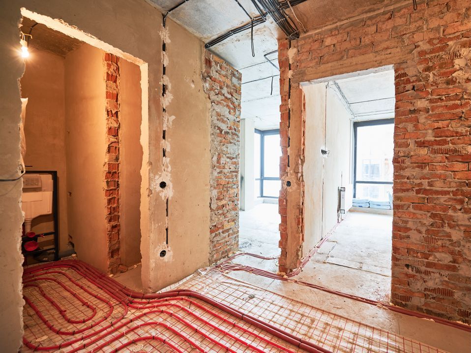 A room under construction with a brick wall and red pipes on the floor.