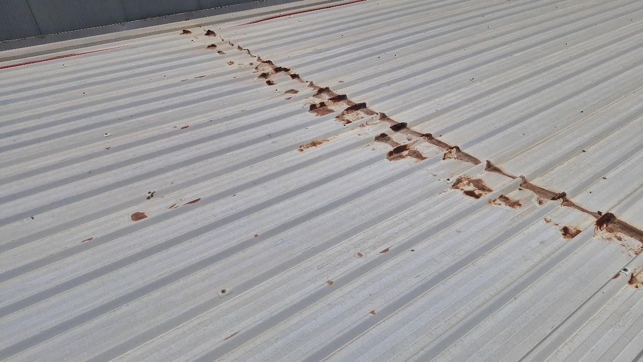 Corrugated metal roof with rust spots along the seam. White panels with parallel ridges.