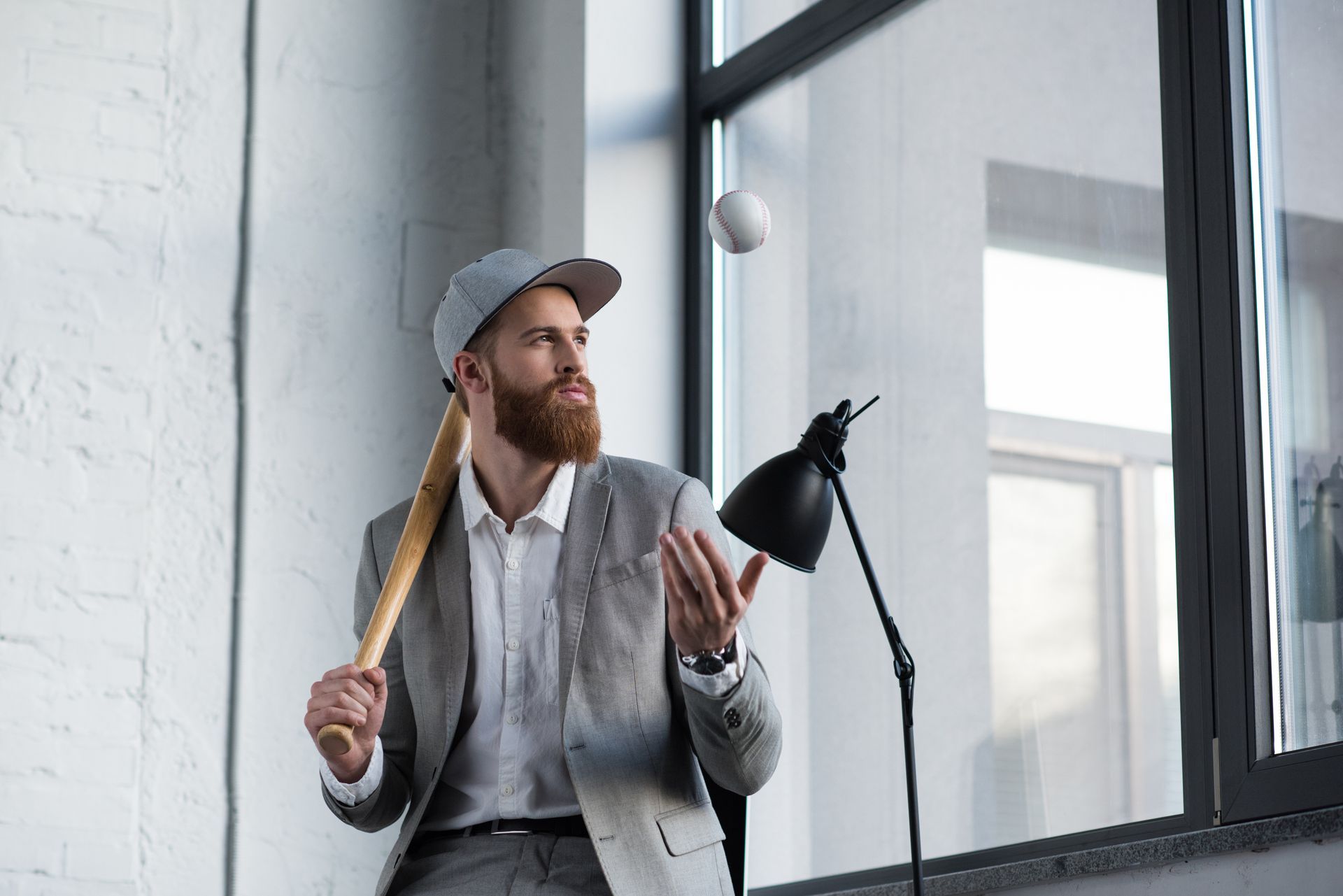 A man in a suit and hat is holding a baseball bat and throwing a ball.