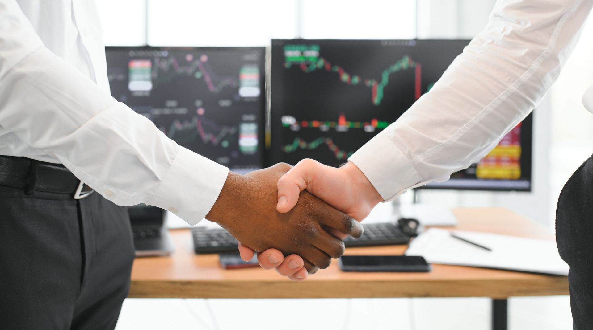 Two men are shaking hands in front of a computer screen.