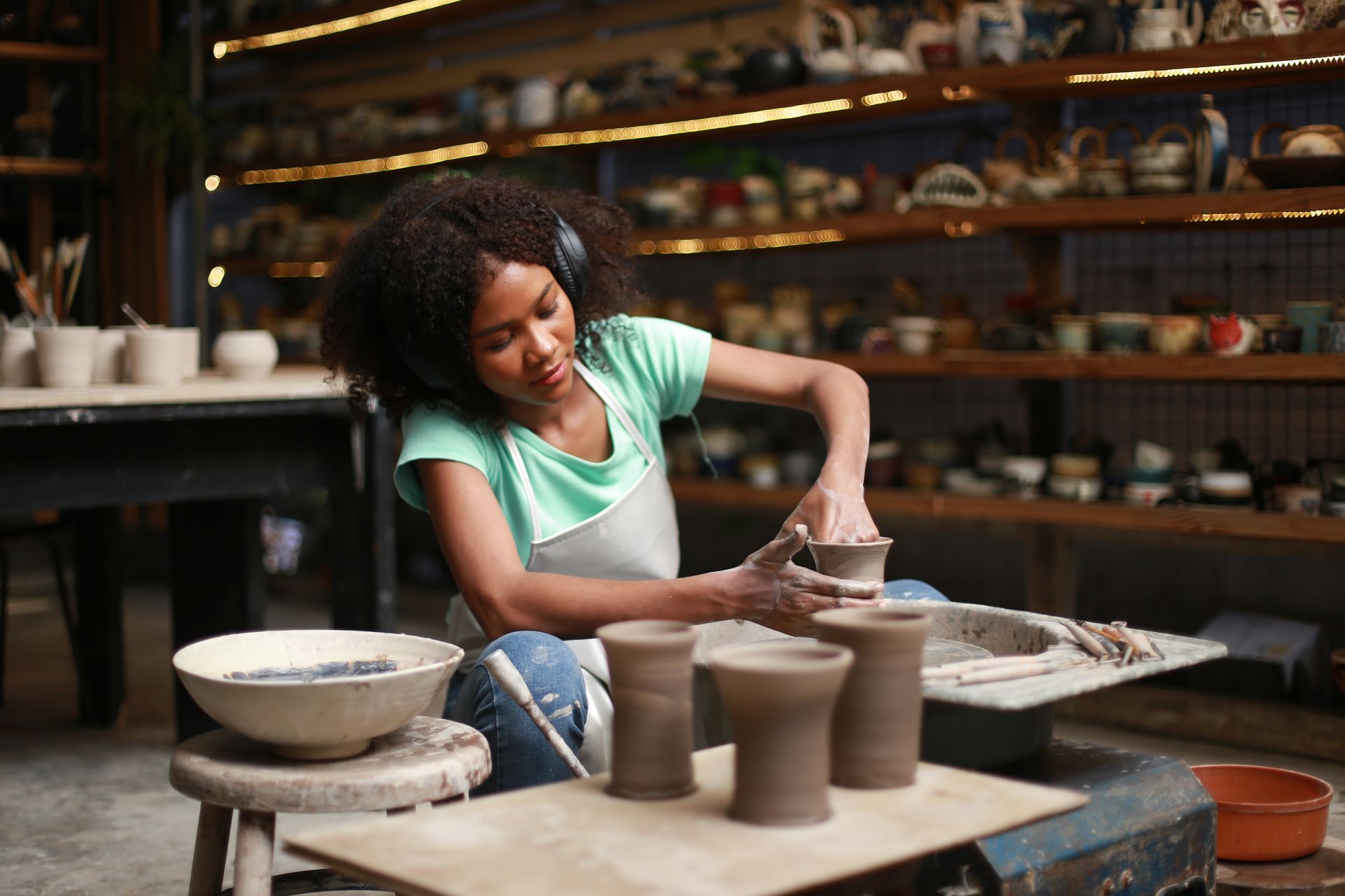 A woman is sitting on a pottery wheel making pots.