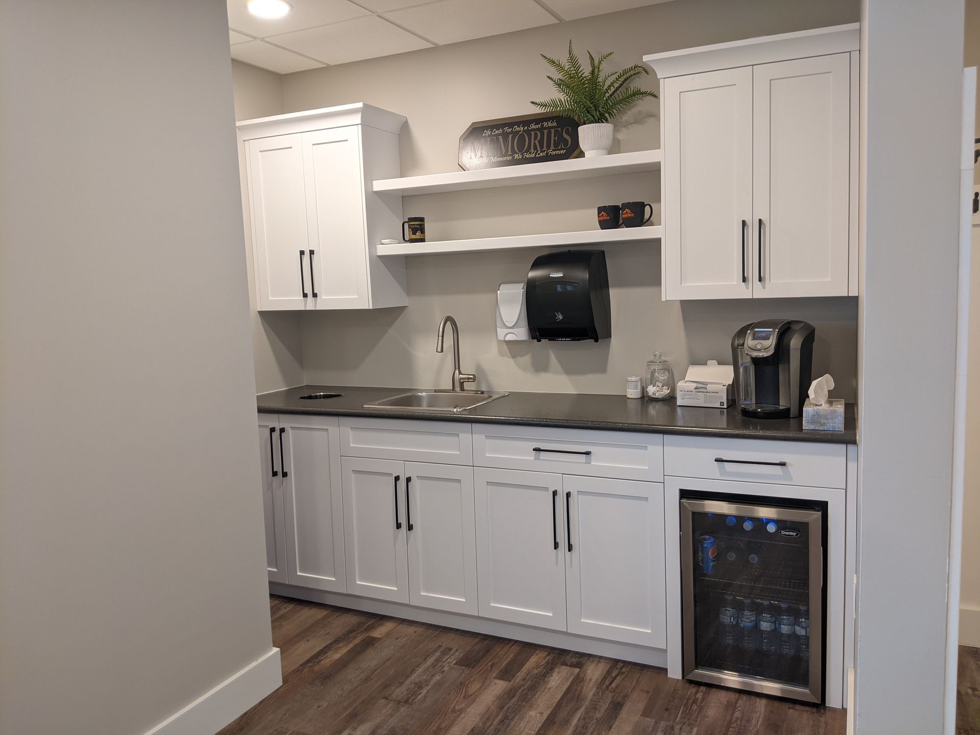 White kitchenette with cabinets, sink, shelves, and a mini-fridge.