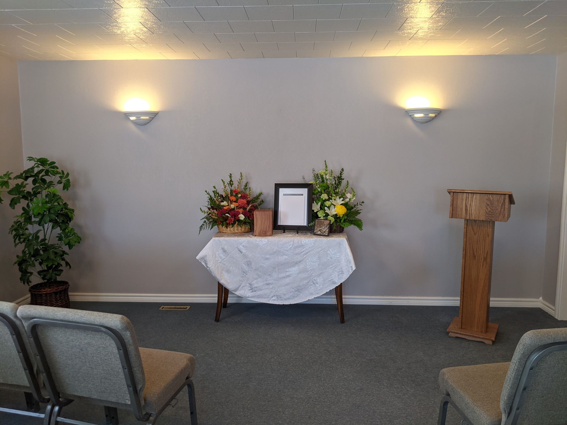 Funeral home interior with floral arrangements, podium, and chairs.