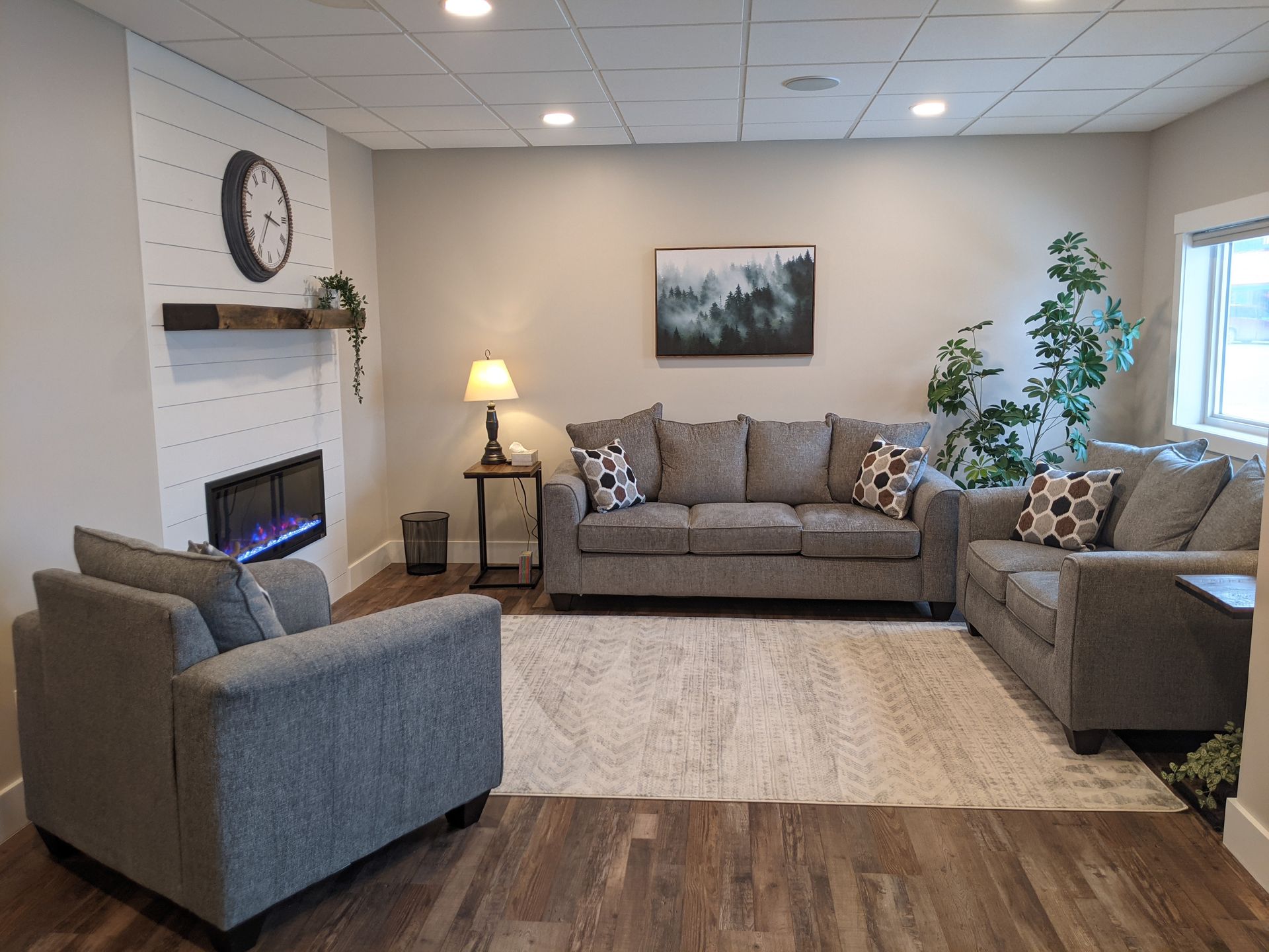 Living room with gray furniture, fireplace, art, and rug on a wood floor.