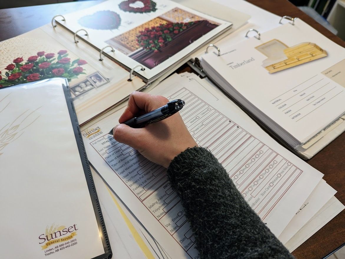 A person's hand writes on a form; floral arrangement samples and a binder are on a table.