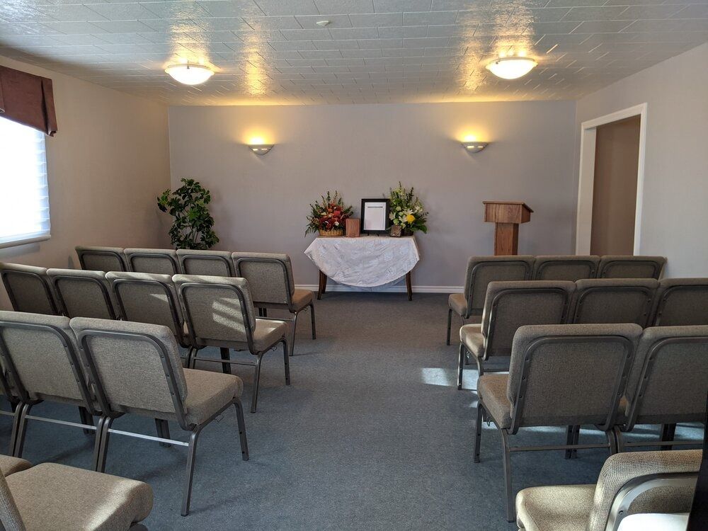 Funeral home chapel with rows of chairs facing a table with flowers and a podium.