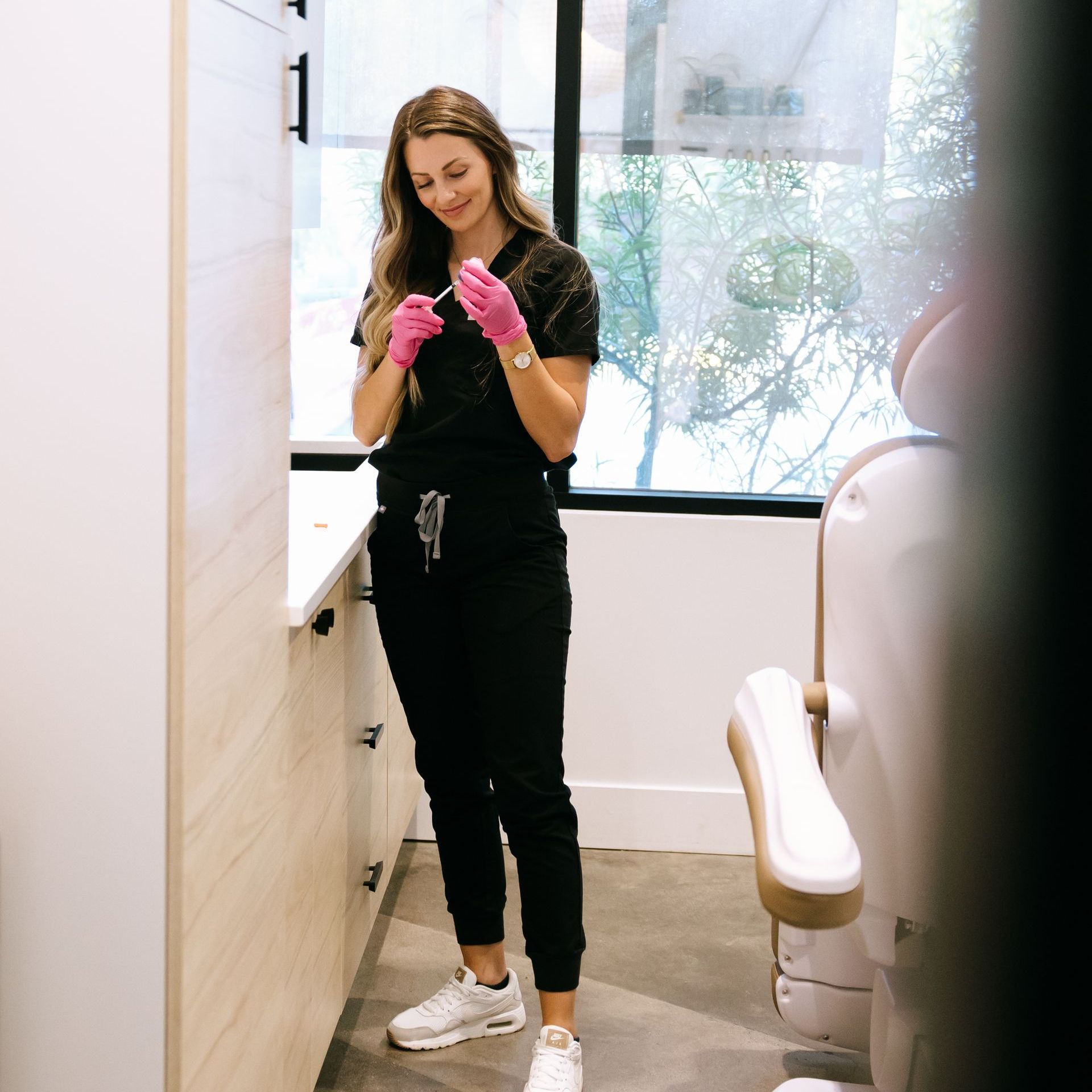 A woman wearing pink gloves is standing in a room next to a window.