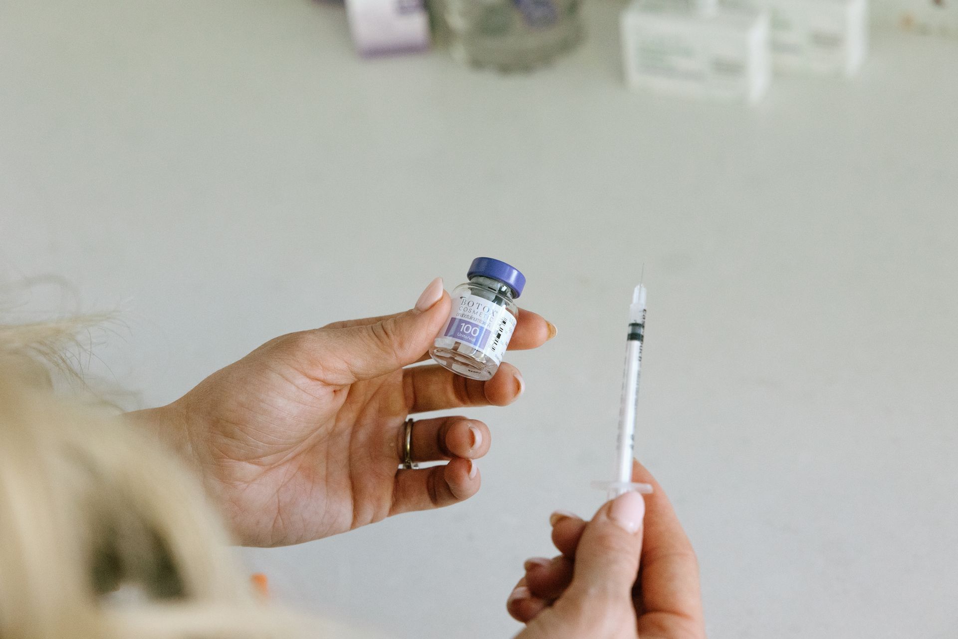 Hands holding a vial and syringe, preparing for an injection.