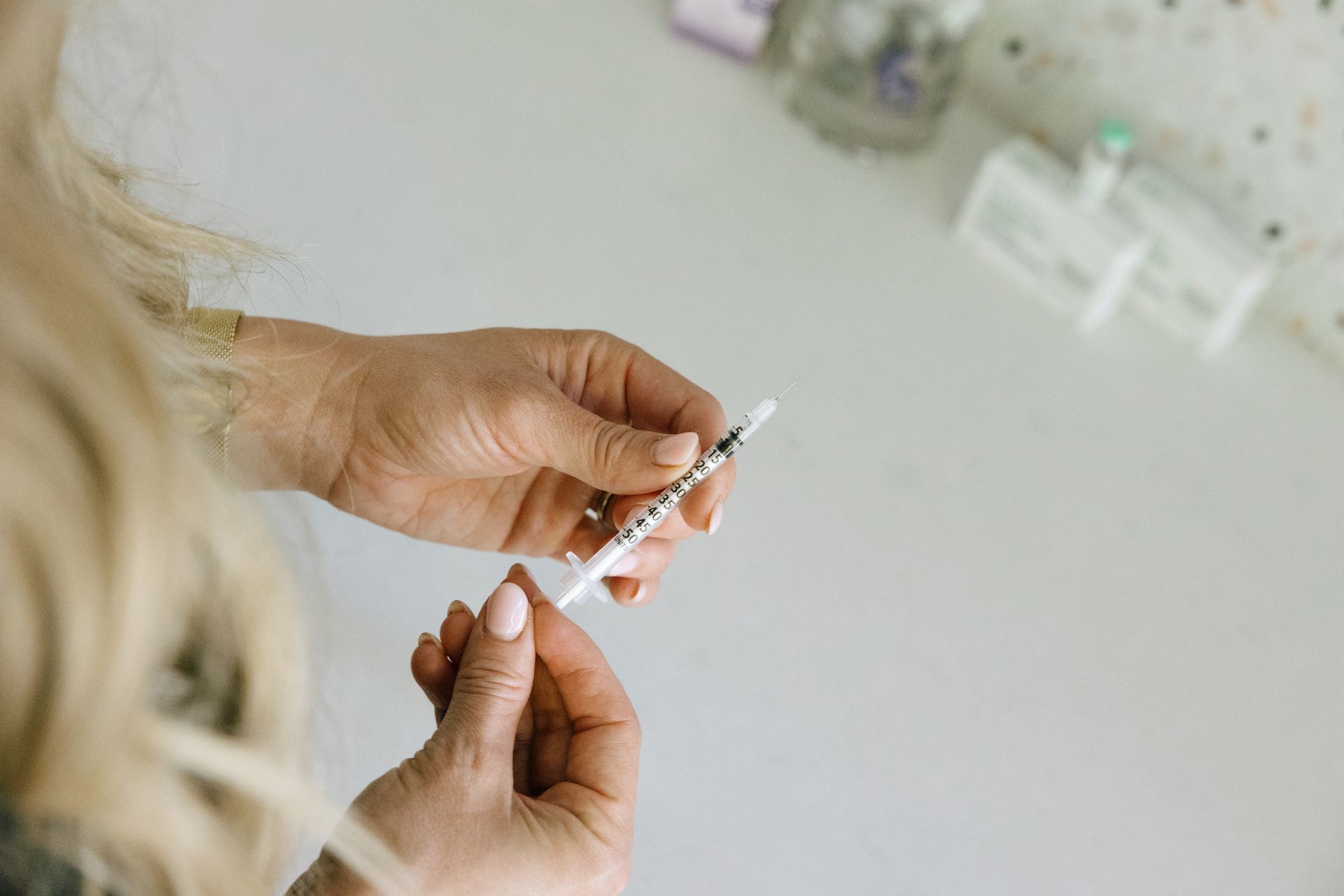 Woman holding syringe, preparing for an injection on a white surface. Blonde hair, clean medical setting.