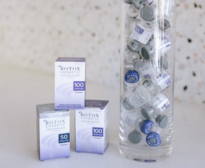 A glass filled with botox bottles and boxes on a table.