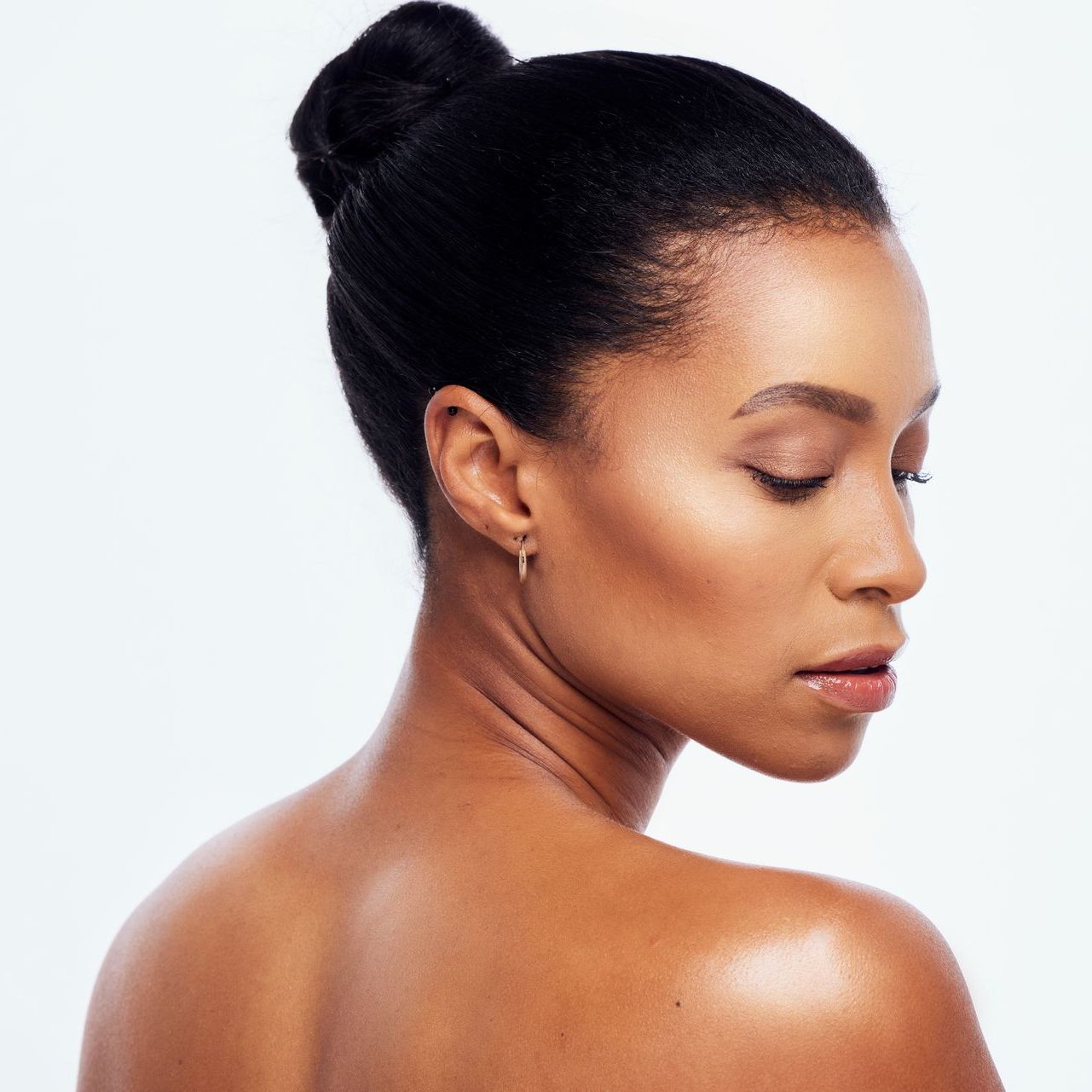 A woman with her hair in a bun is looking over her shoulder.