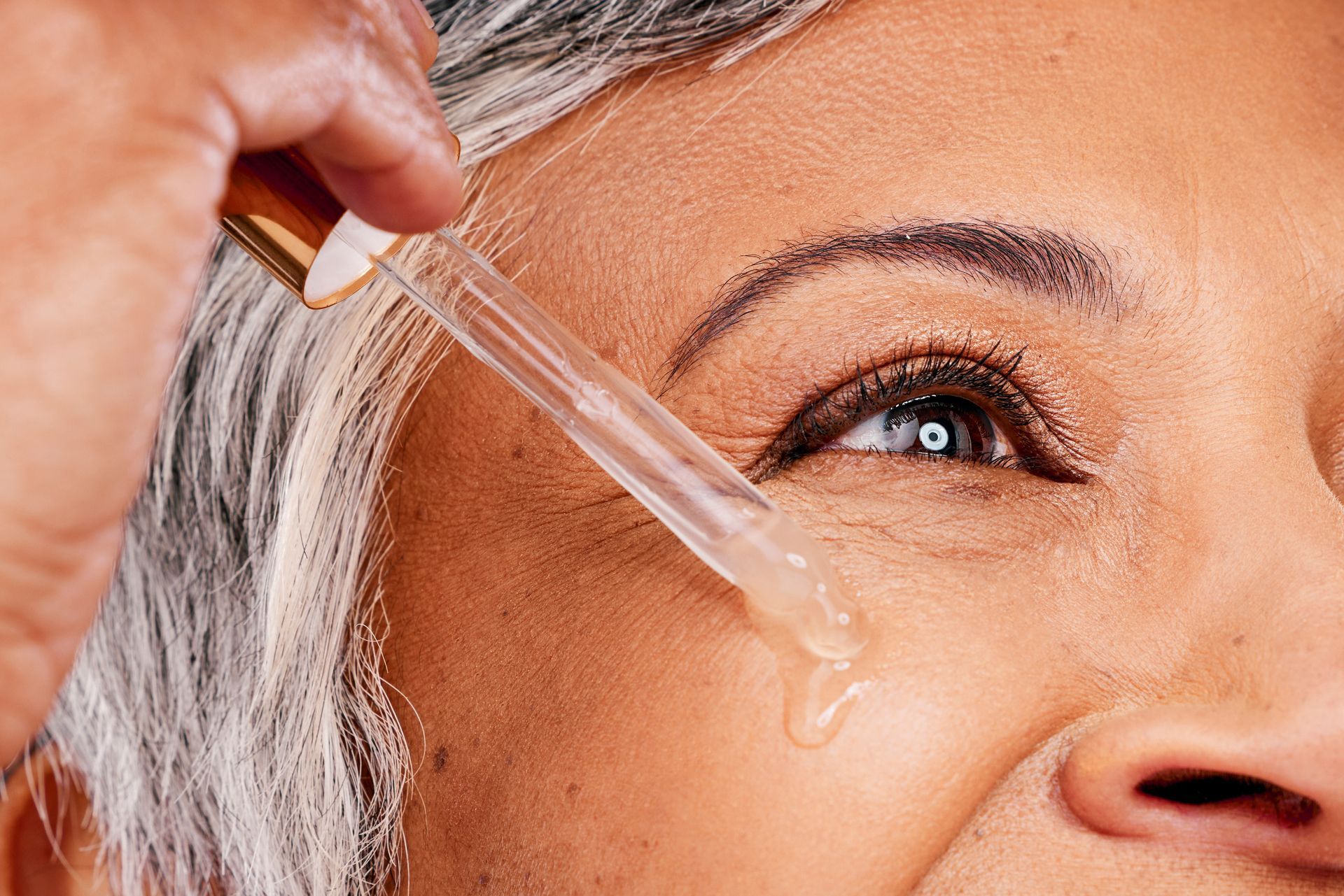 A woman is applying a serum to her face with a pipette.