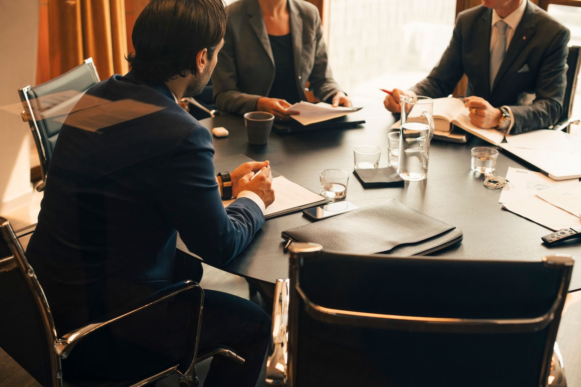 Business meeting in a conference room with three people seated around a table, discussing documents.