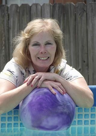 A woman is leaning on a purple bowling ball and smiling.