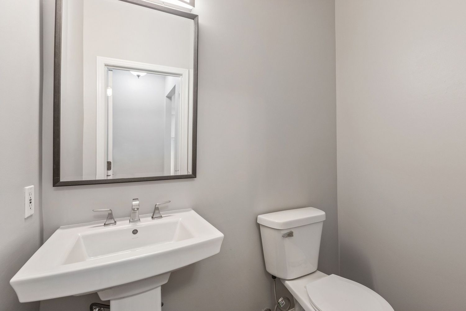 Gray-walled bathroom with a white pedestal sink, toilet, and mirror.