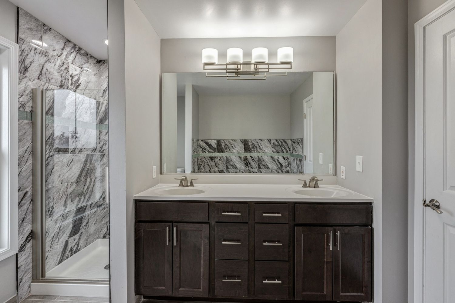 Bathroom with a dark wood double vanity, large mirror, marble shower, and white door.