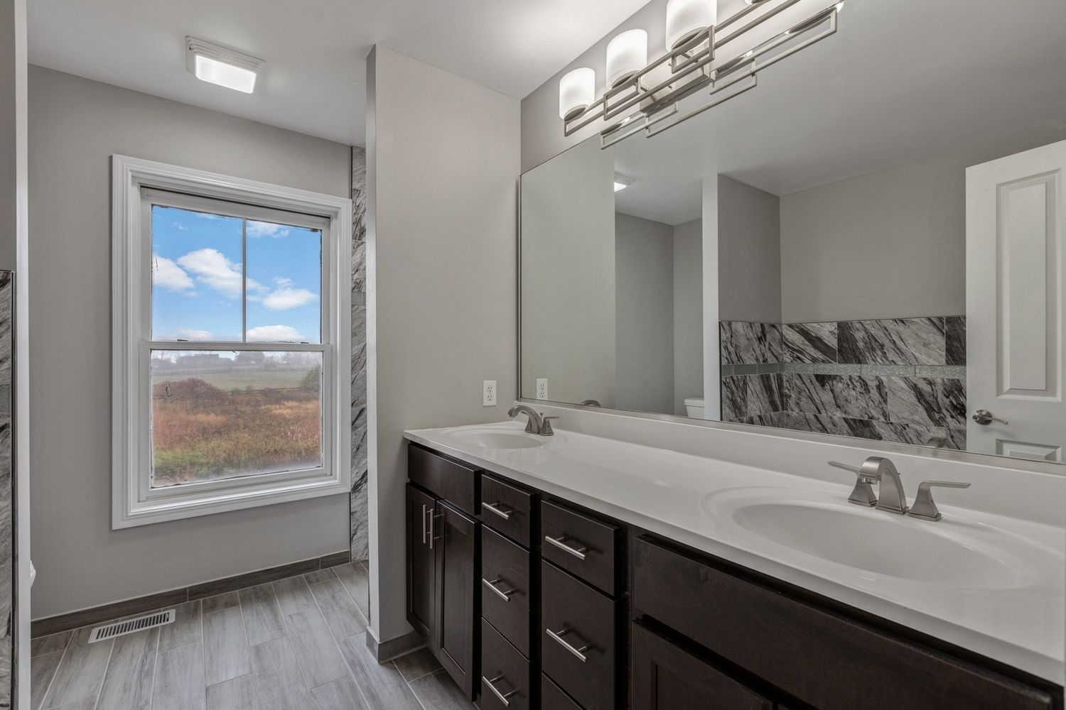 Bathroom with dark cabinets, white countertop, large mirror, window with outside view.