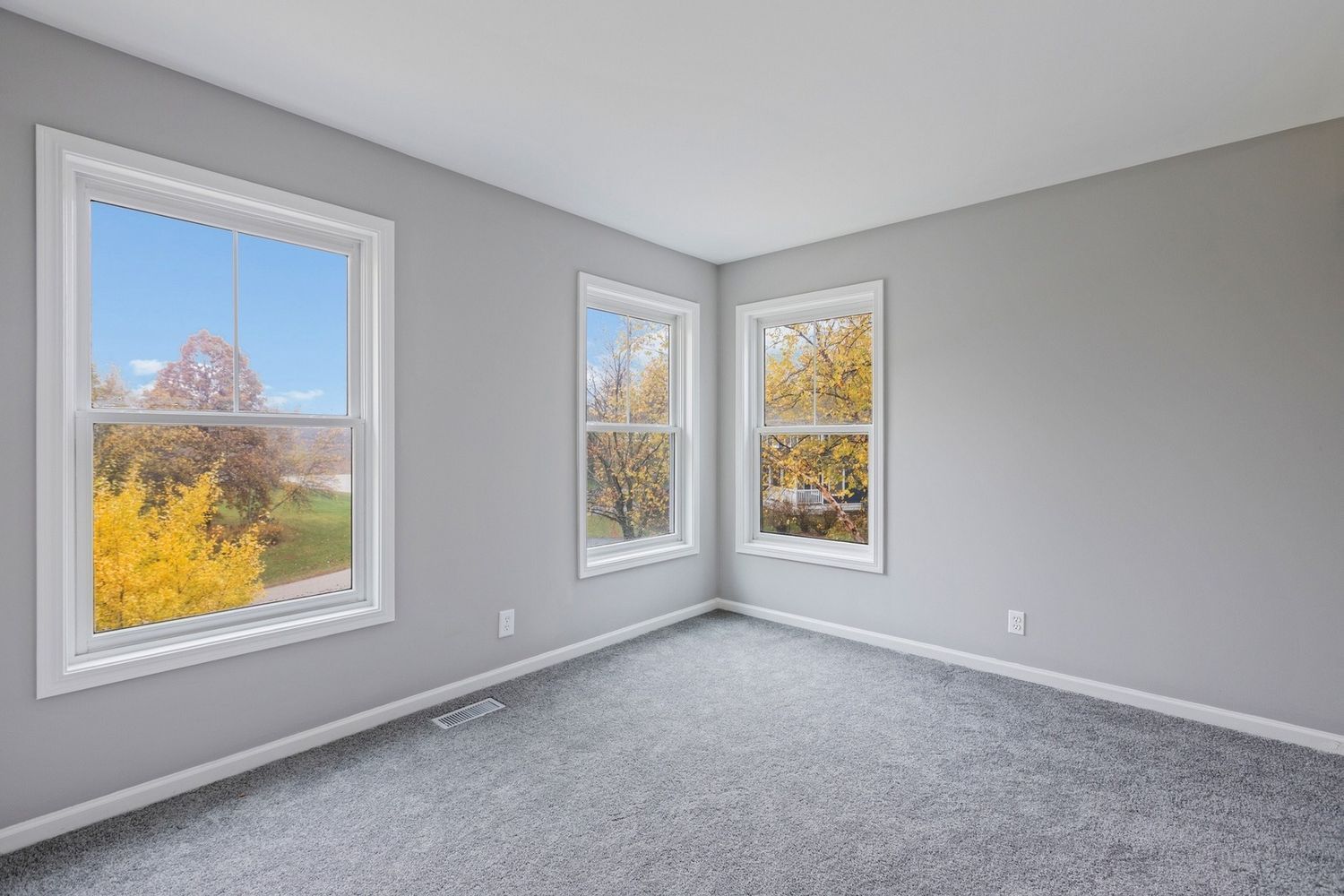 Empty room with gray walls, carpet, and three windows with outdoor views.